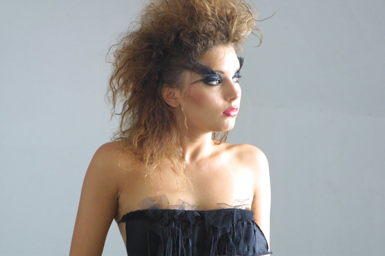 Striking portrait of a woman with dramatic makeup and voluminous hairstyle wearing a black dress.